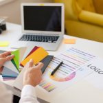 Hands of a designer sitting and choosing colors from the template card. Horizontal indoors shot.