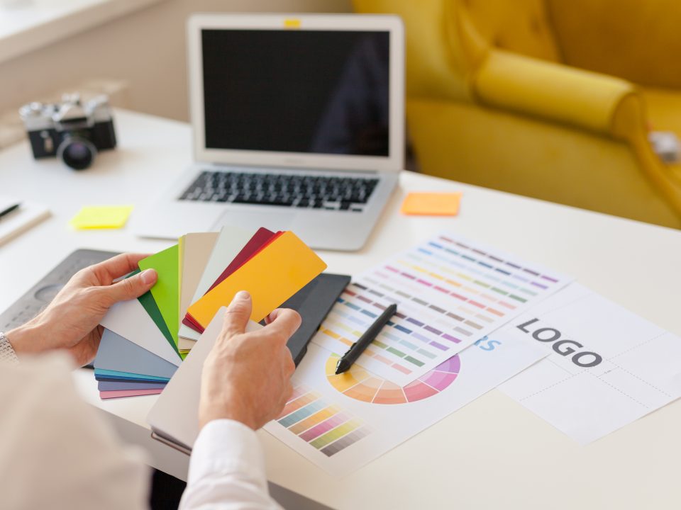 Hands of a designer sitting and choosing colors from the template card. Horizontal indoors shot.