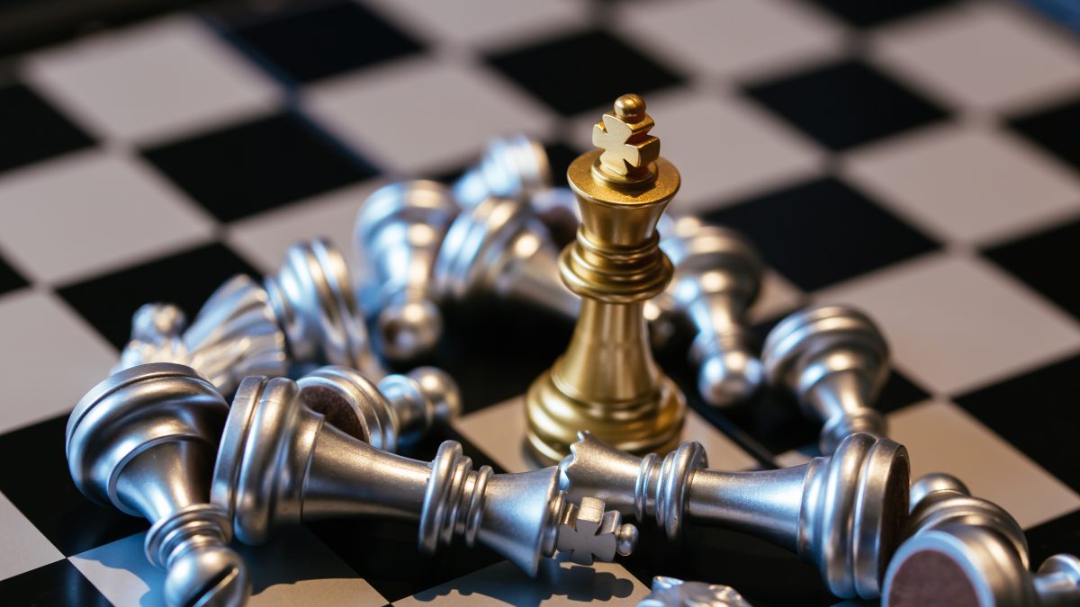 Set of silver chess pieces placed on board around golden king after defeat