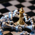 Set of silver chess pieces placed on board around golden king after defeat